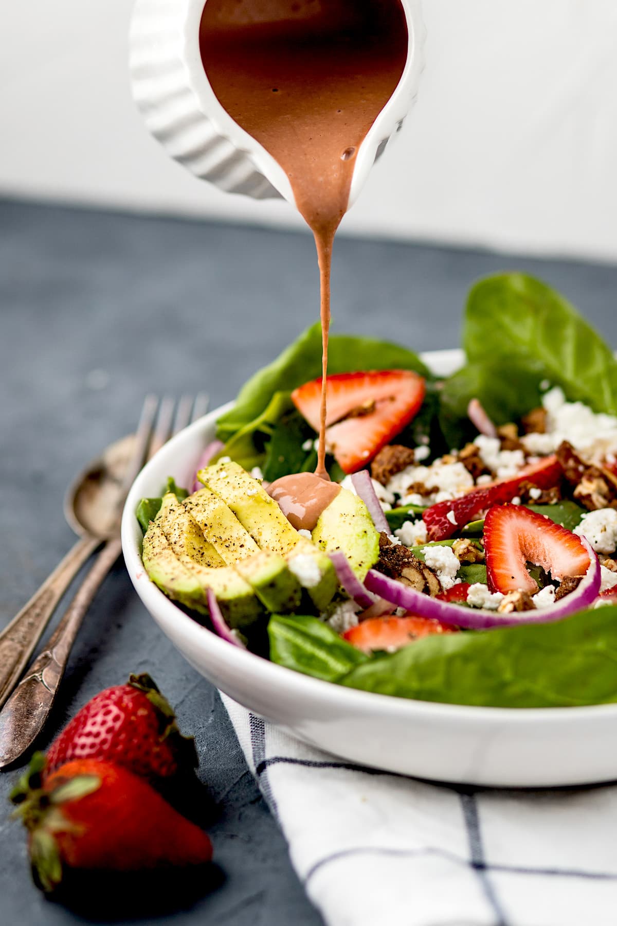 strawberry spinach salad in white serving bowl with dressing being poured on top.