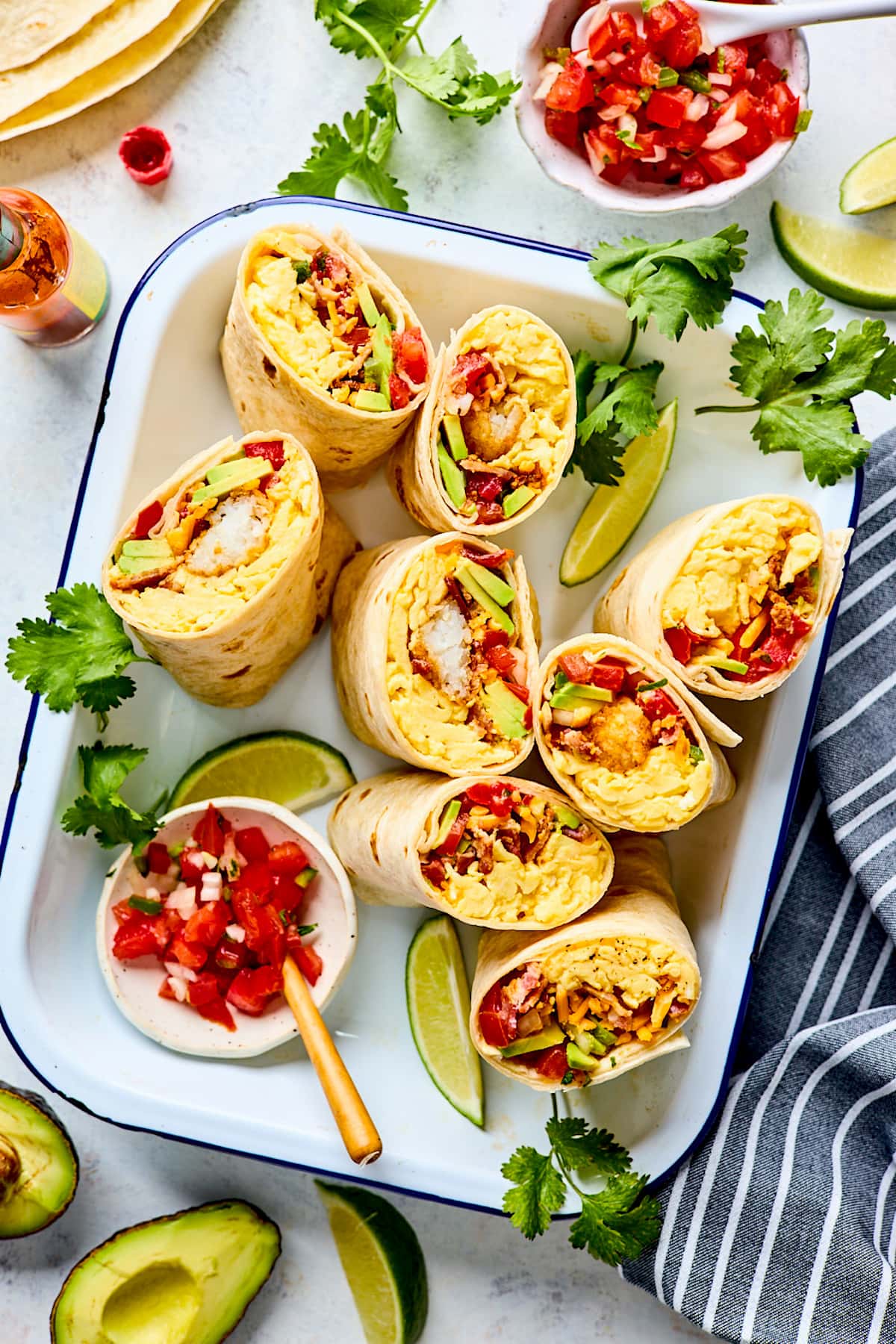 breakfast burritos cut in half on large tray with pico de gallo and cilantro.