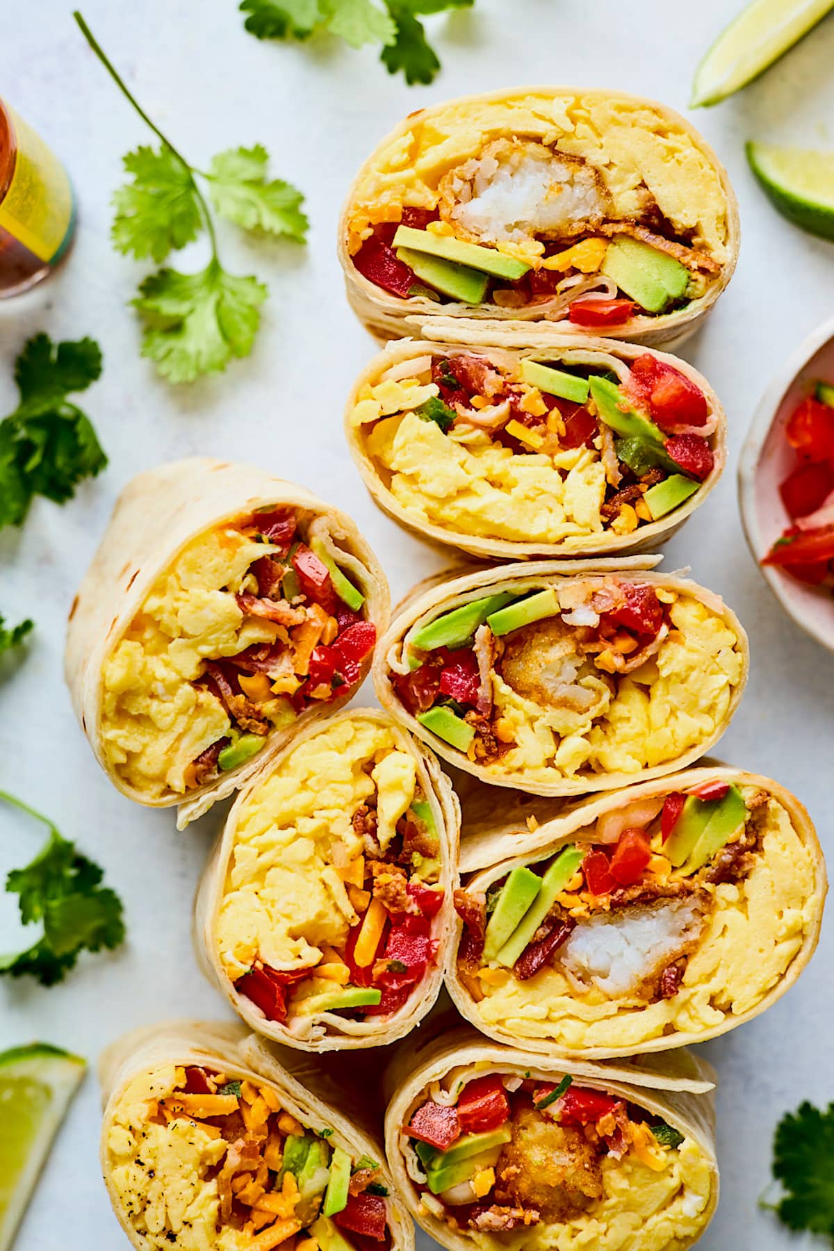 breakfast burritos with eggs. bacon, cheese, tater tots, avocado, and pico de gallo in flour tortillas.