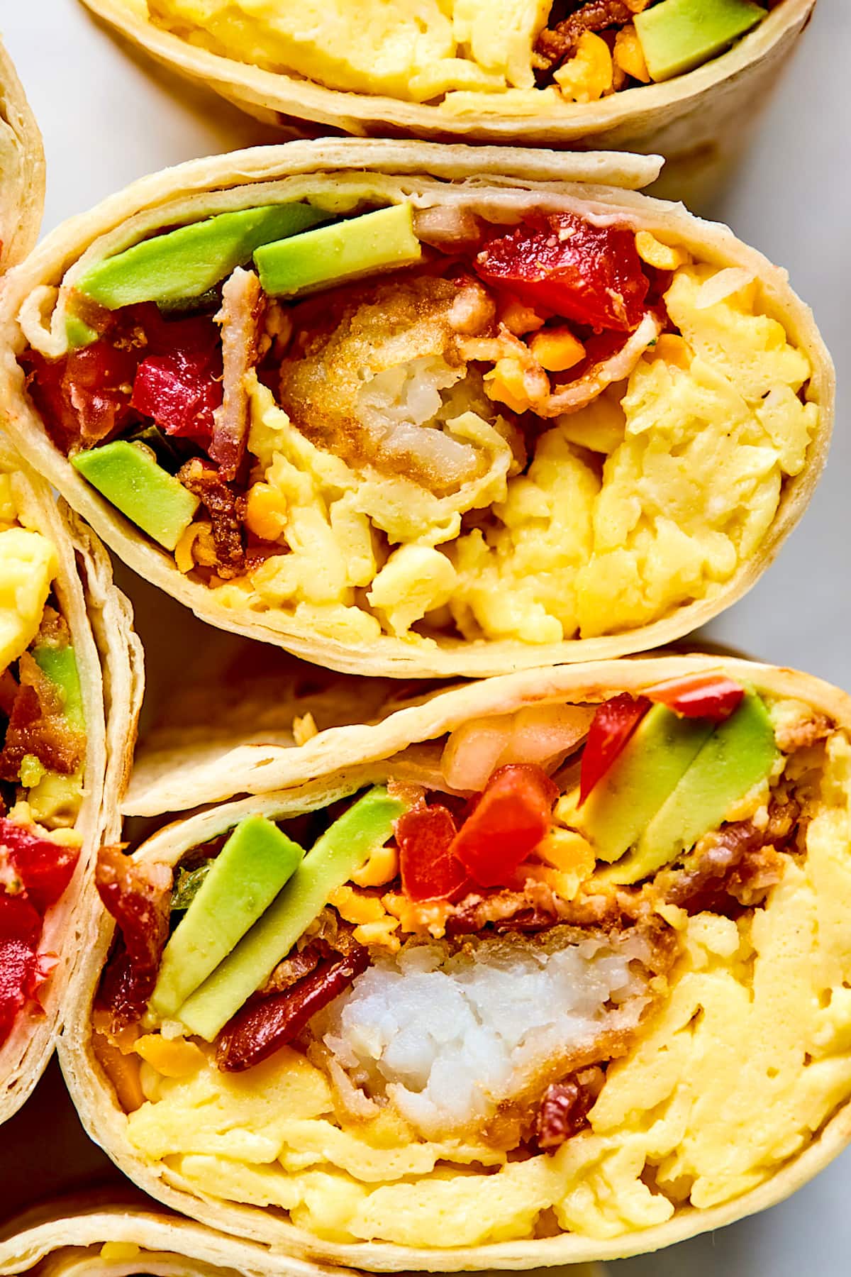 breakfast burritos with scrambled eggs, tater togs, bacon, cheese, avocado, and pico de gallo.