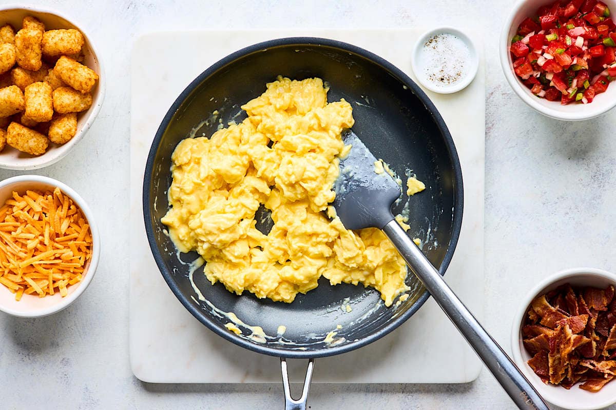 scrambled eggs cooking in skillet with spatula.