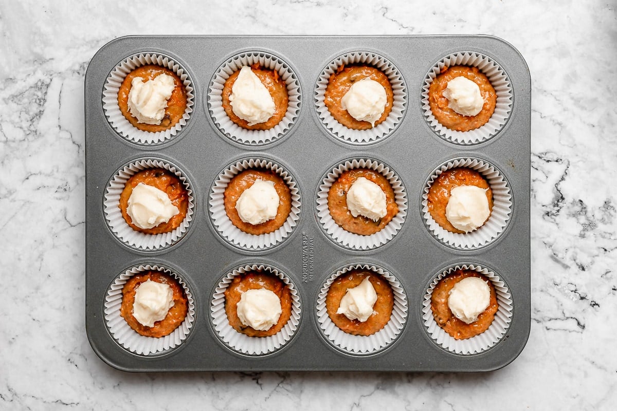 carrot cake muffin batter with cream cheese filling in muffin pan.