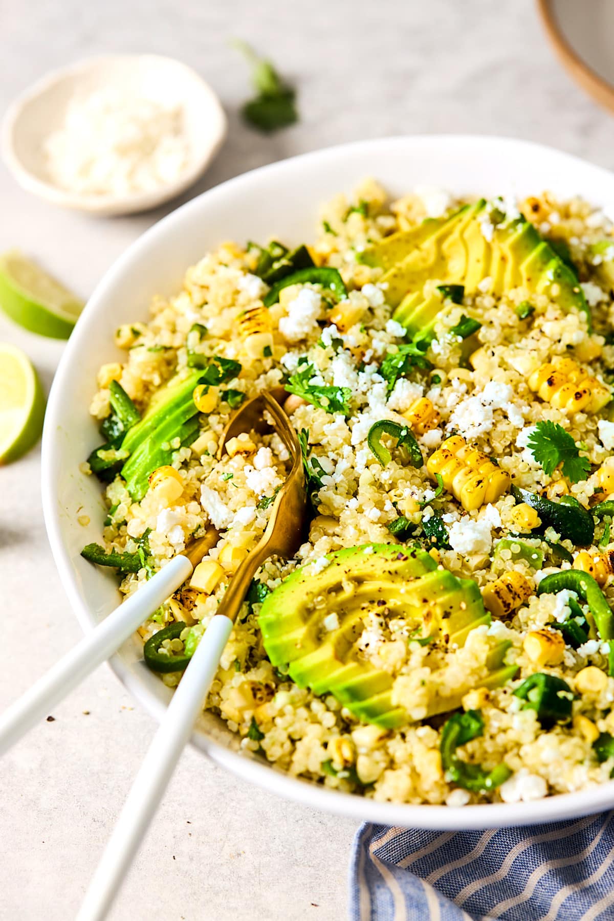 charred corn and avocado quinoa salad recipe in white bowl with serving spoons.