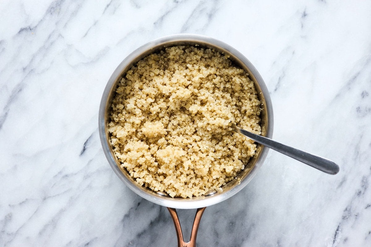 cooked quinoa in pot with fork to fluff it.