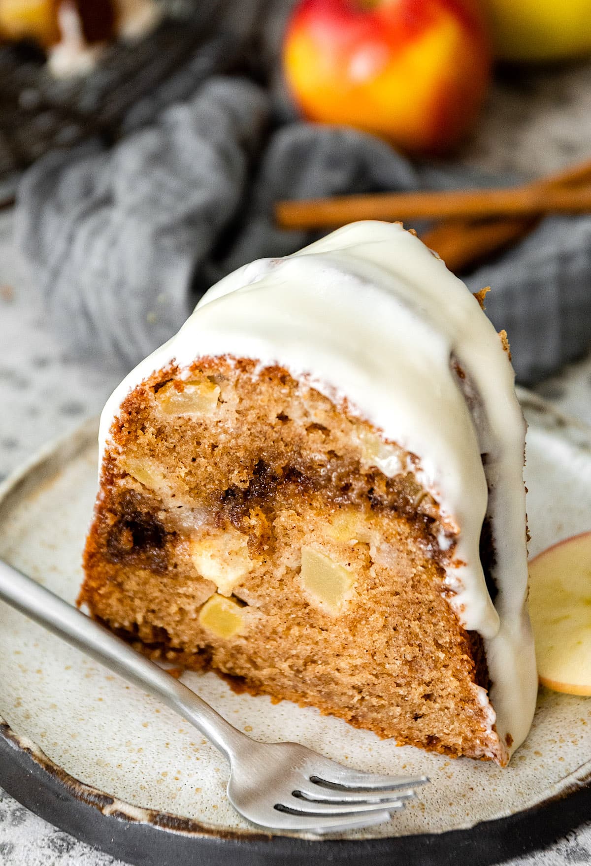 piece of apple bundt cake with cream cheese frosting on plate with fork. 