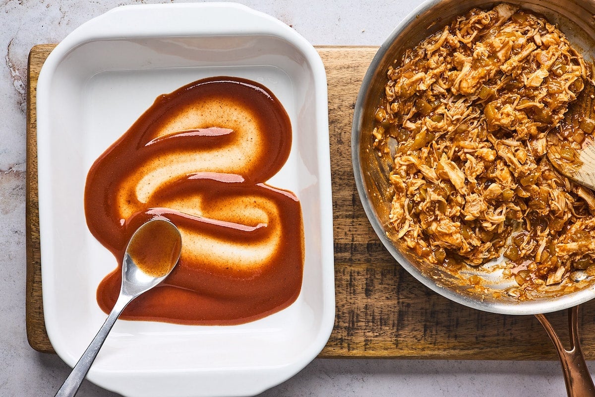 chicken enchilada sauce being spread in baking dish with chicken enchilada filling in skillet.