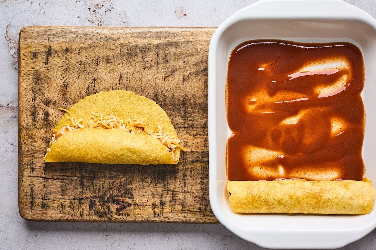 rolling chicken enchiladas and putting them in baking dish with enchilada sauce.