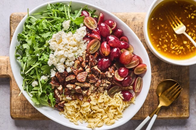 orzo salad with grapes, arugula, feta cheese, candied pecans in a bowl with balsamic vinaigrette.