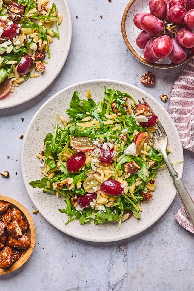 orzo salad with grapes, arugula. feta cheese, candied pecans on plate with fork.