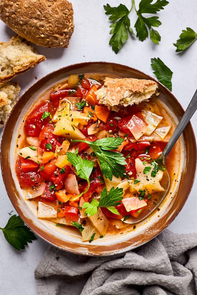 cabbage soup in bowl with crusty bread and parsley with spoon.