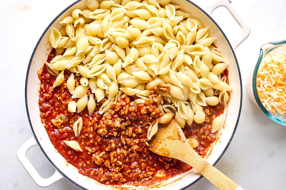 making taco pasta in skillet with pasta shells and taco meat sauce.