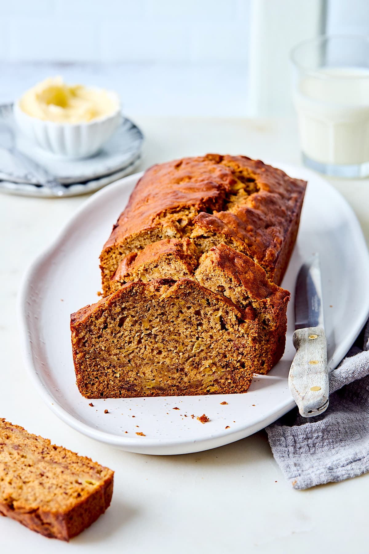 loaf of banana bread cut in slices on platter with knife.