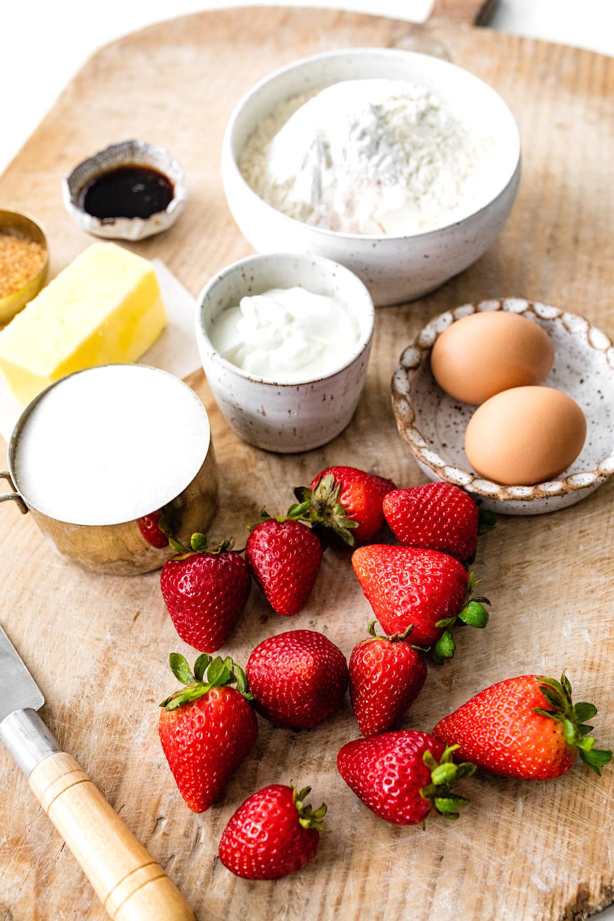 strawberry muffin ingredients in bowls and fresh strawberries on wood board.