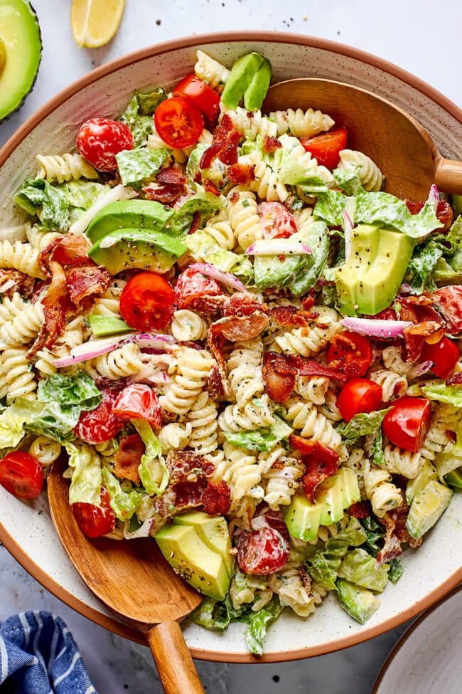 BLT pasta salad in bowl with wood serving spoons.