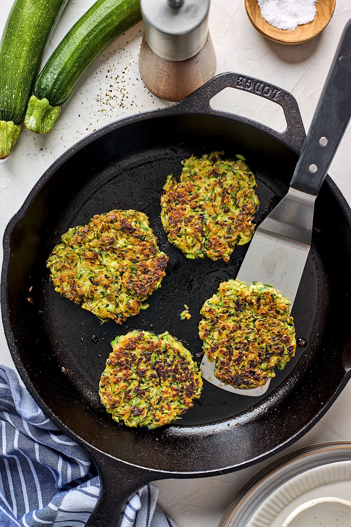 zucchini fritters in cast iron skillet with spatula.
