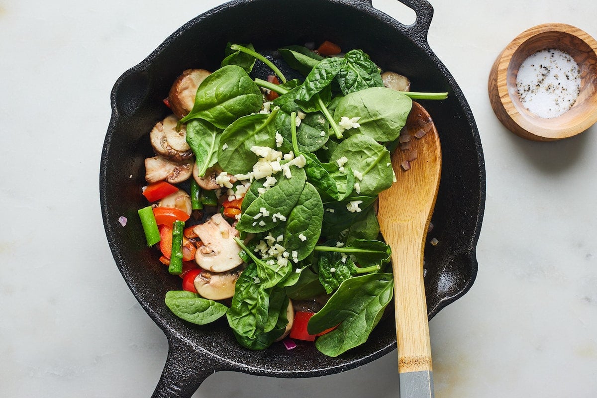 vegetables in cast iron skillet with wooden spoon.