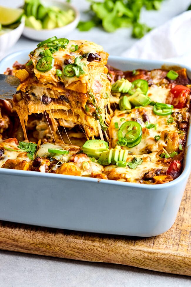 lifting a piece of stacked vegetable enchilada out of the pan with a spatula.