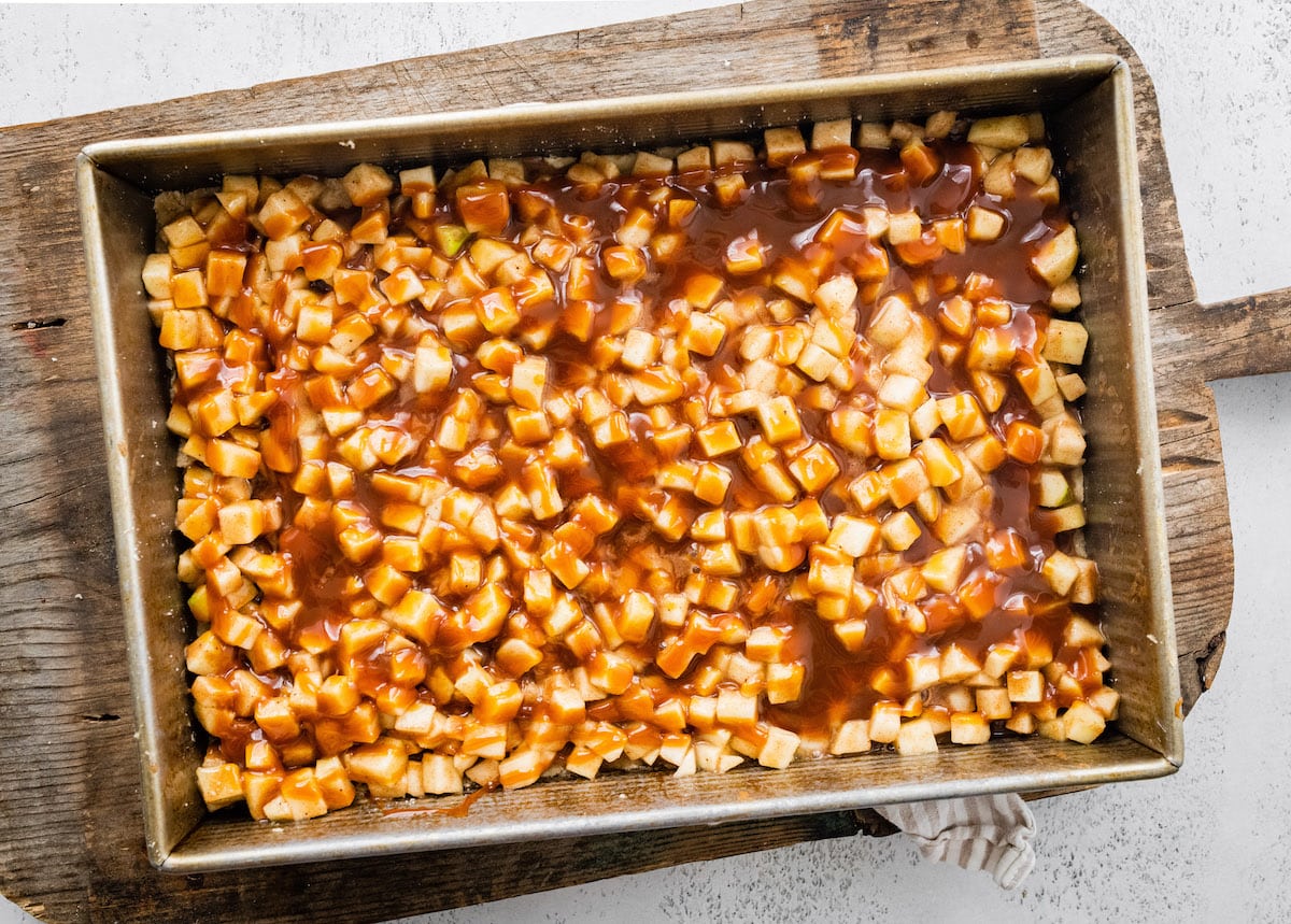 diced apples spread over crust and drizzled with salted caramel sauce in a 9x13-inch pan.