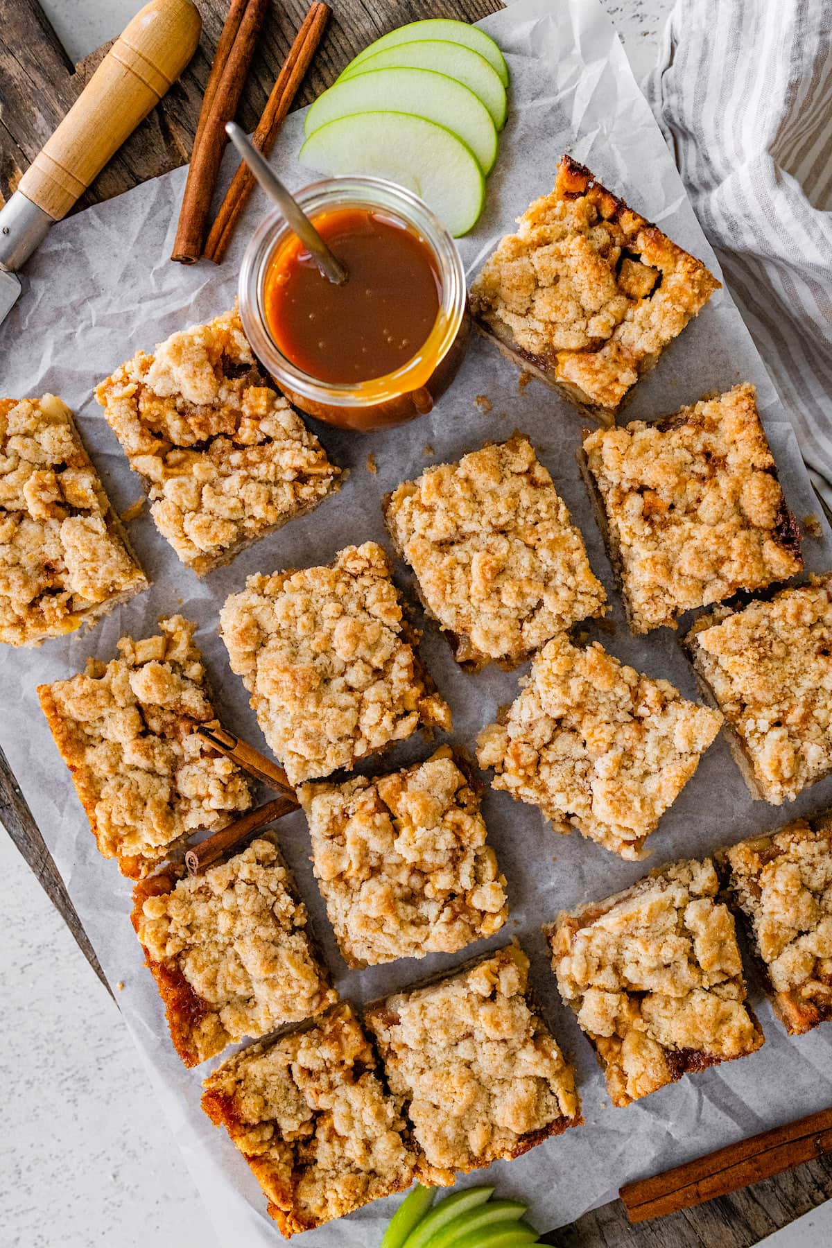 salted caramel apple crumb bars cut into squares on a wood cutting board with parchment paper.