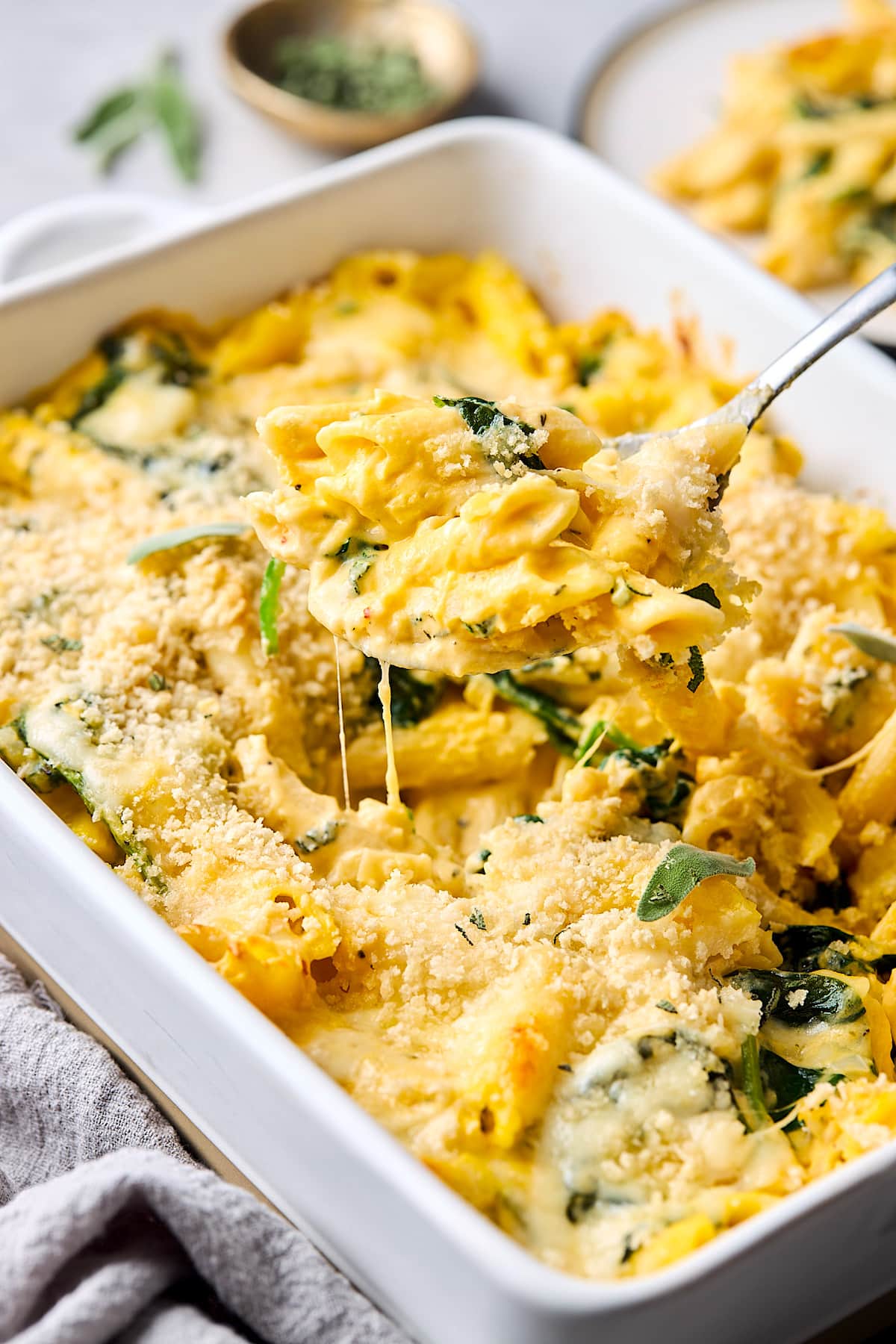 Butternut squash baked ziti in baking dish with a spoon serving a cheesy portion.