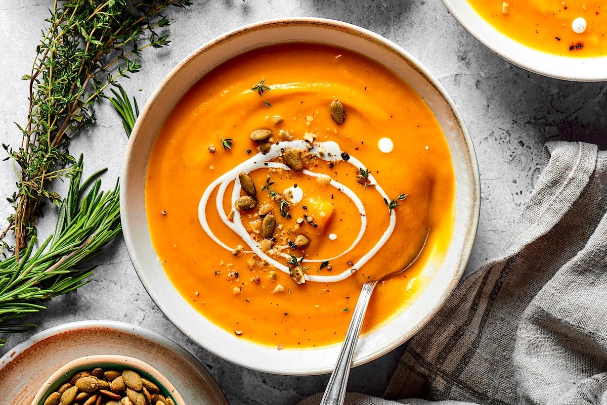 butternut squash soup in bowl with toppings and fresh herbs and napkin on the side.