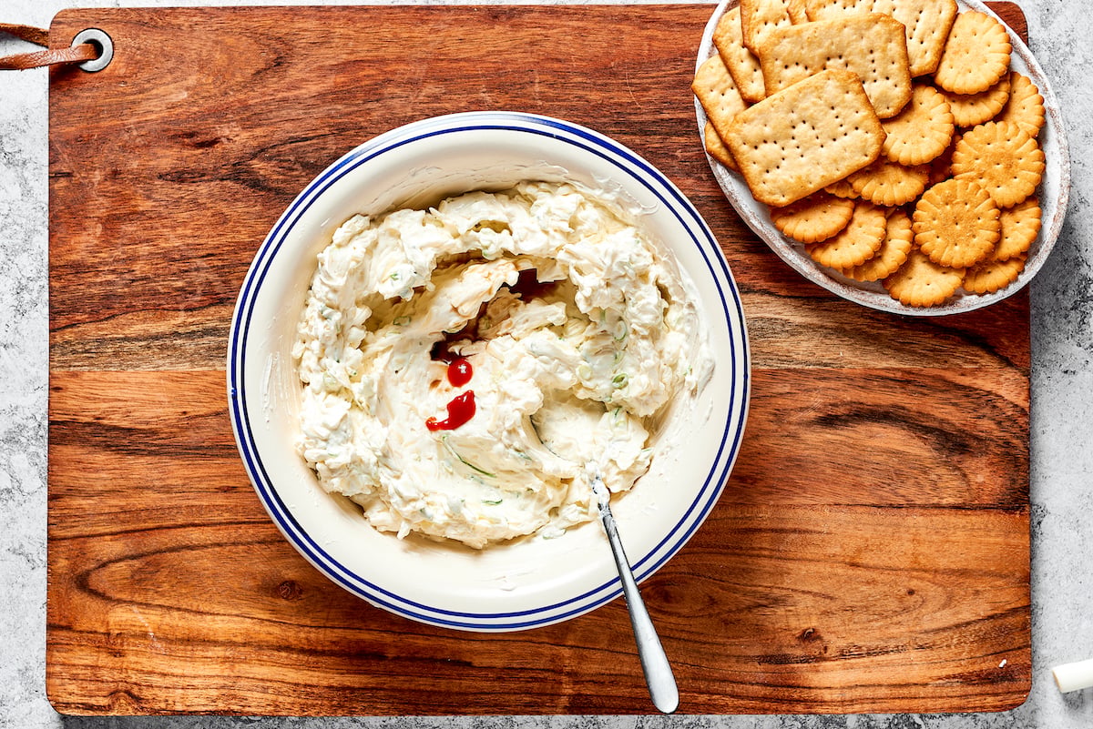 cheese ball mixture in bowl with spoon with a plate of crackers on the side.
