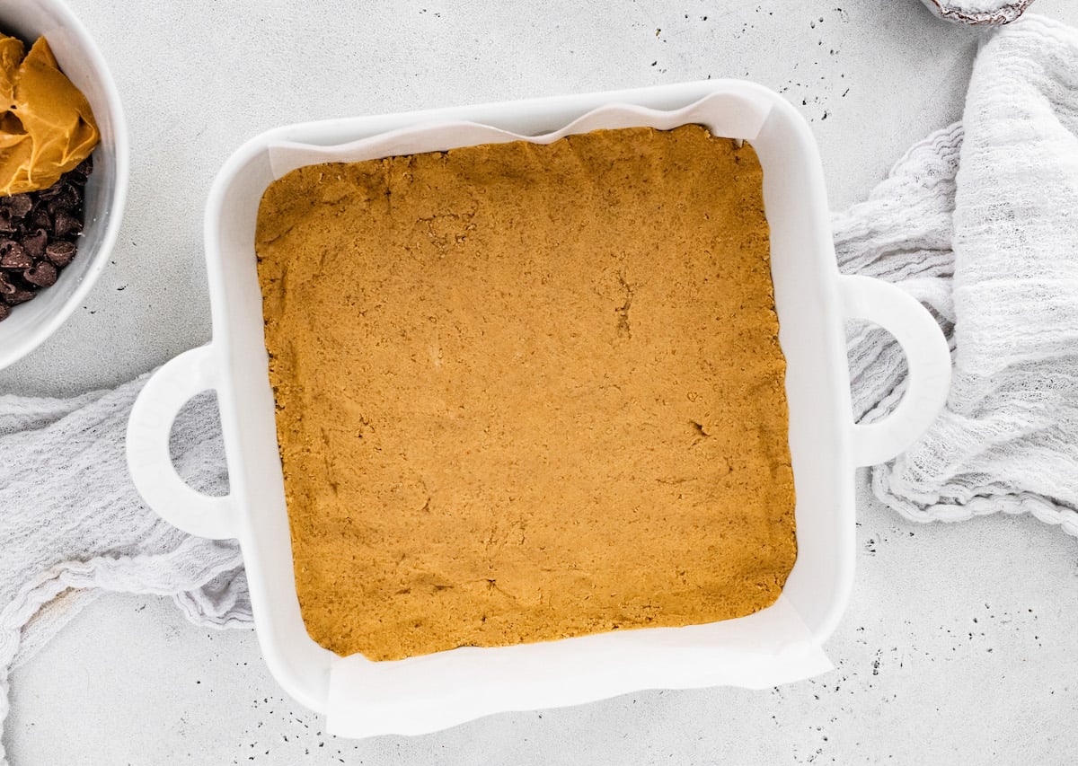 no bake peanut butter bar base pressed in baking dish with parchment paper.
