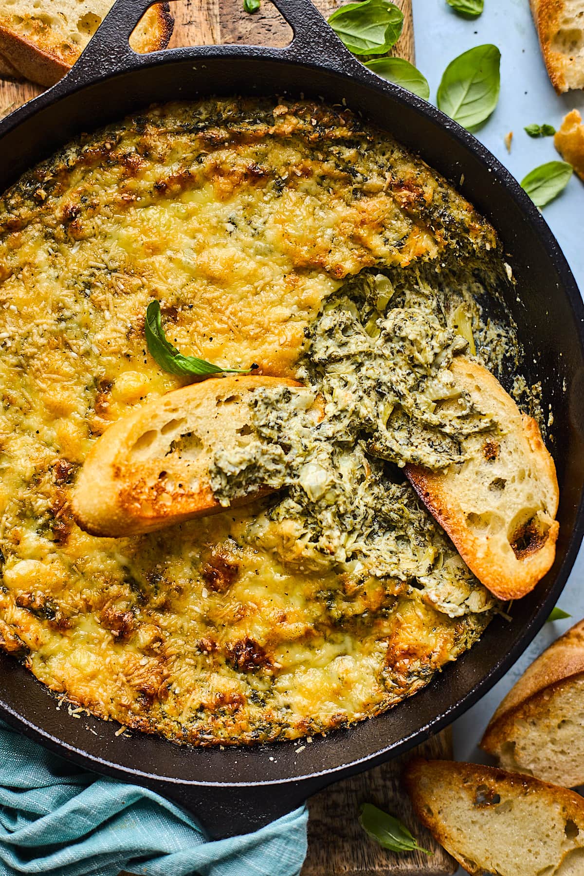 spinach artichoke dip in cast iron skillet with toasted baguette slices.