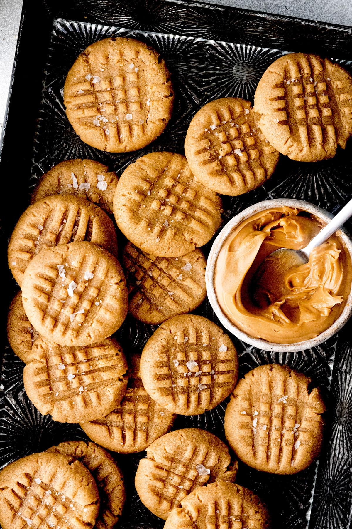 3 ingredient peanut butter cookies with criss cross pattern on baking pan with a jar of peanut butter.