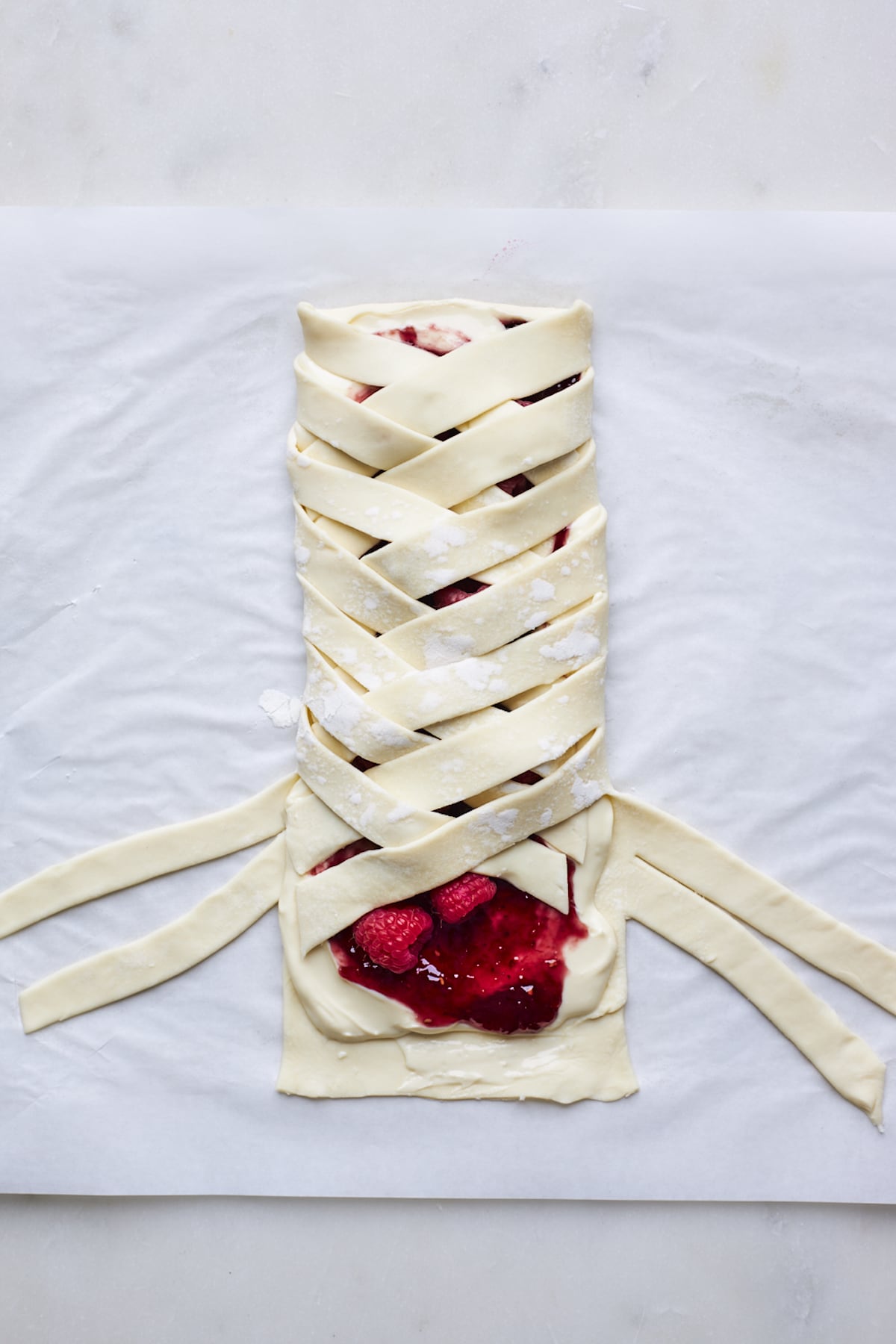 raspberry cream cheese breakfast bread made with puff pastry being braided on parchment paper.