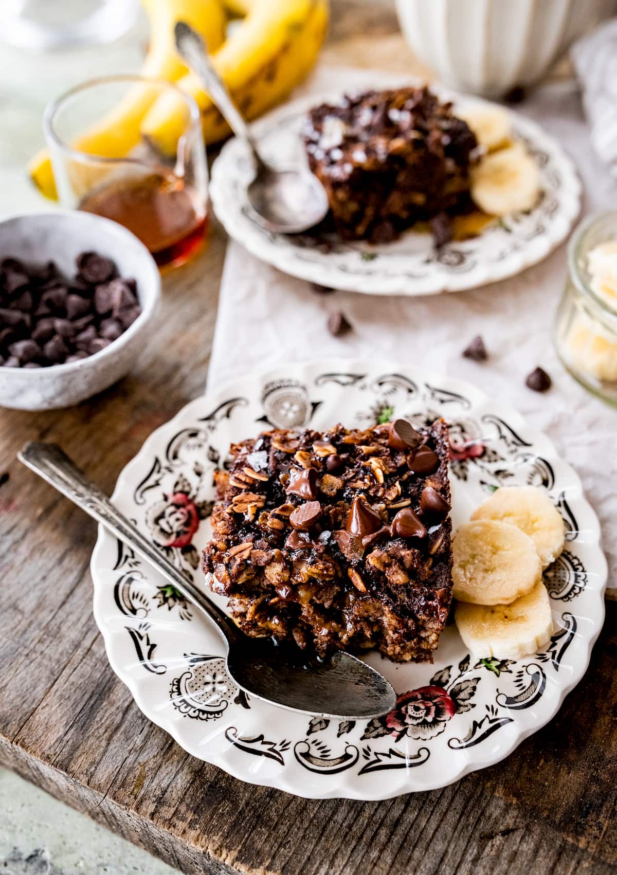 chocolate banana baked oatmeal square on plate with spoon and banana slices.