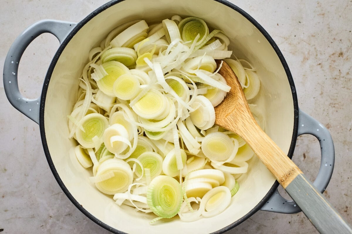leeks sautéing in large pot with wooden spoon.