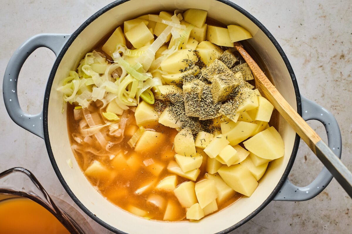 potato leek soup ingredients in large pot with wooden spoon.