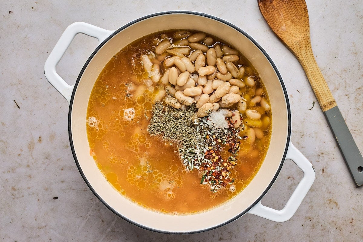 white beans with vegetable broth and spices in large white pot with wooden spoon.