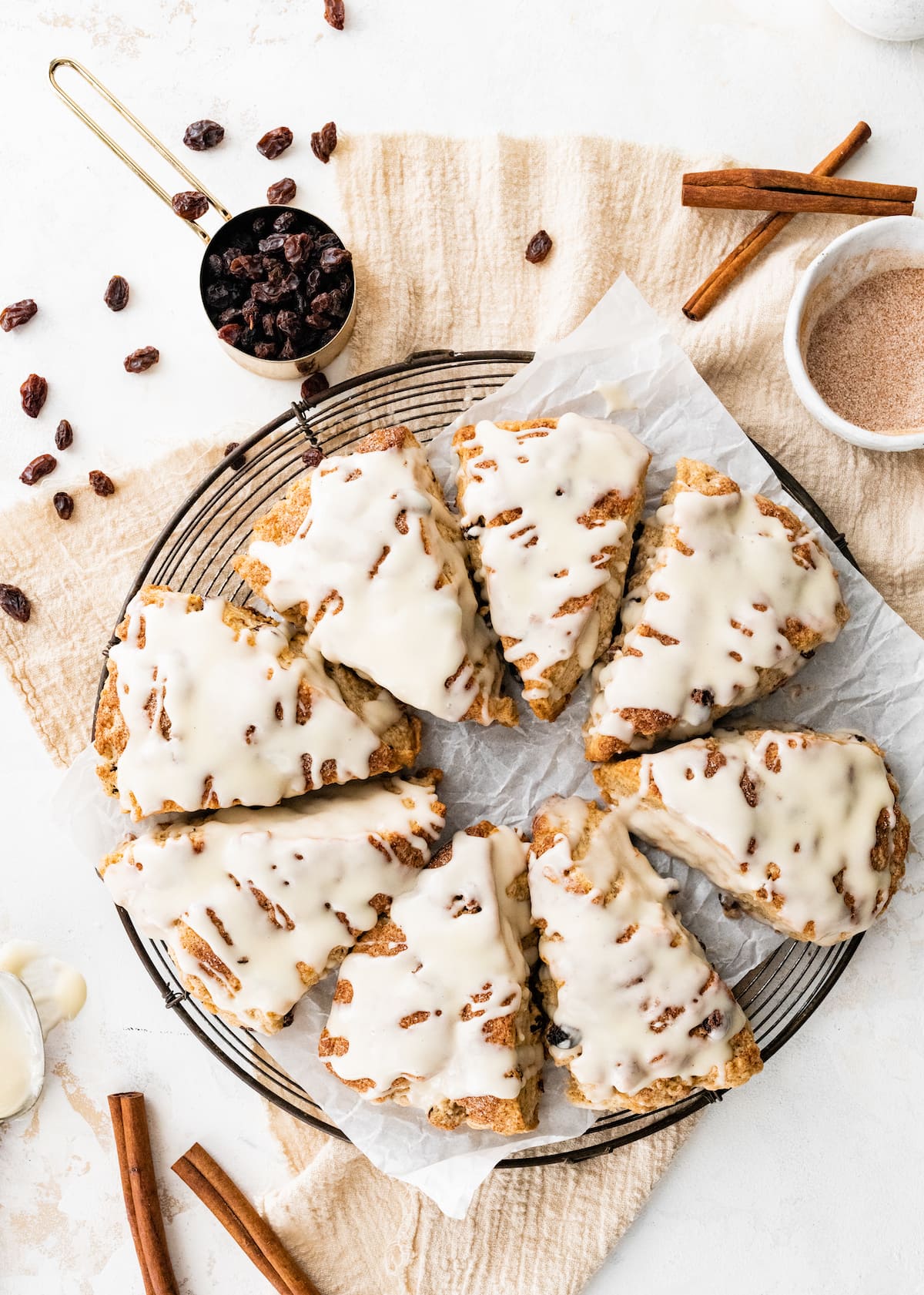 cinnamon raisin scones with vanilla glaze on cooling rack with parchment paper.