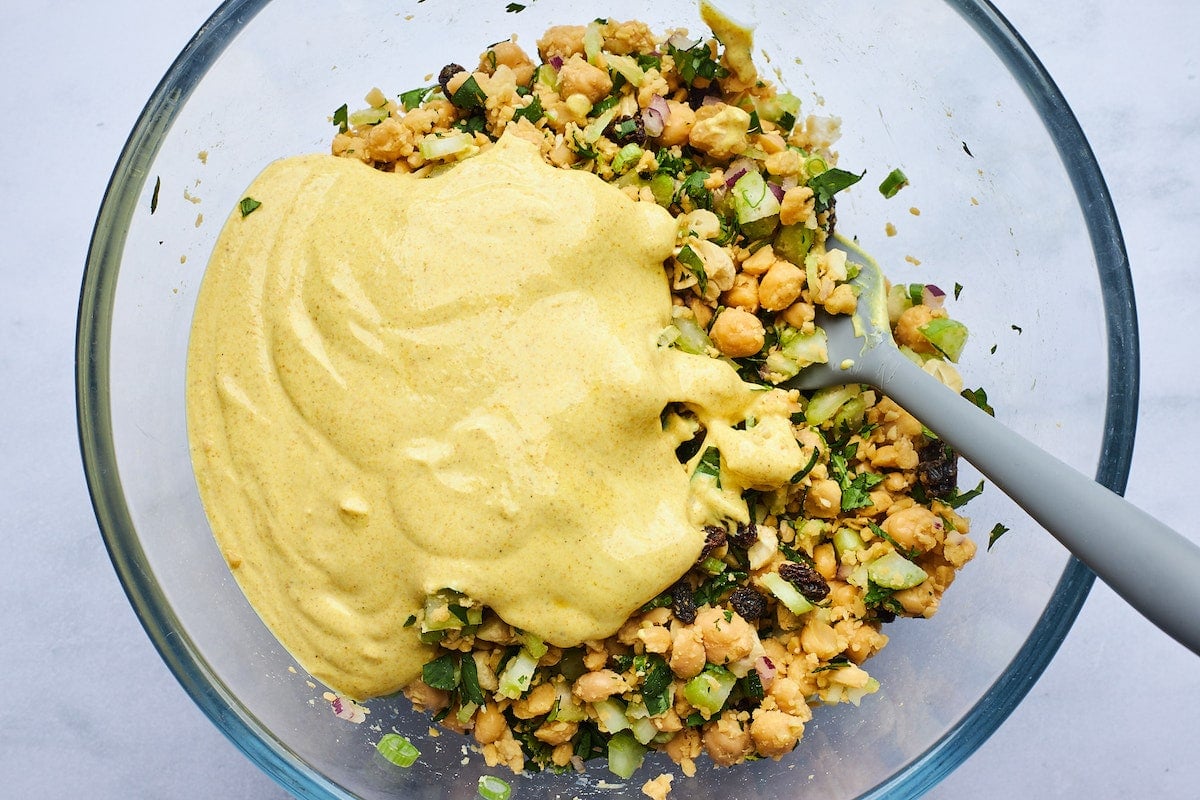 curried chickpea salad in bowl with creamy curry dressing and spatula.