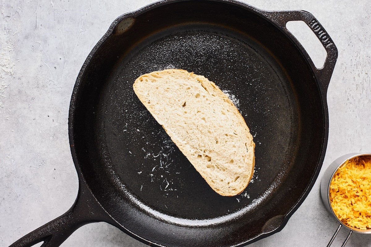 slice of bread in a hot cast iron skillet with parmesan cheese to make grilled cheese.