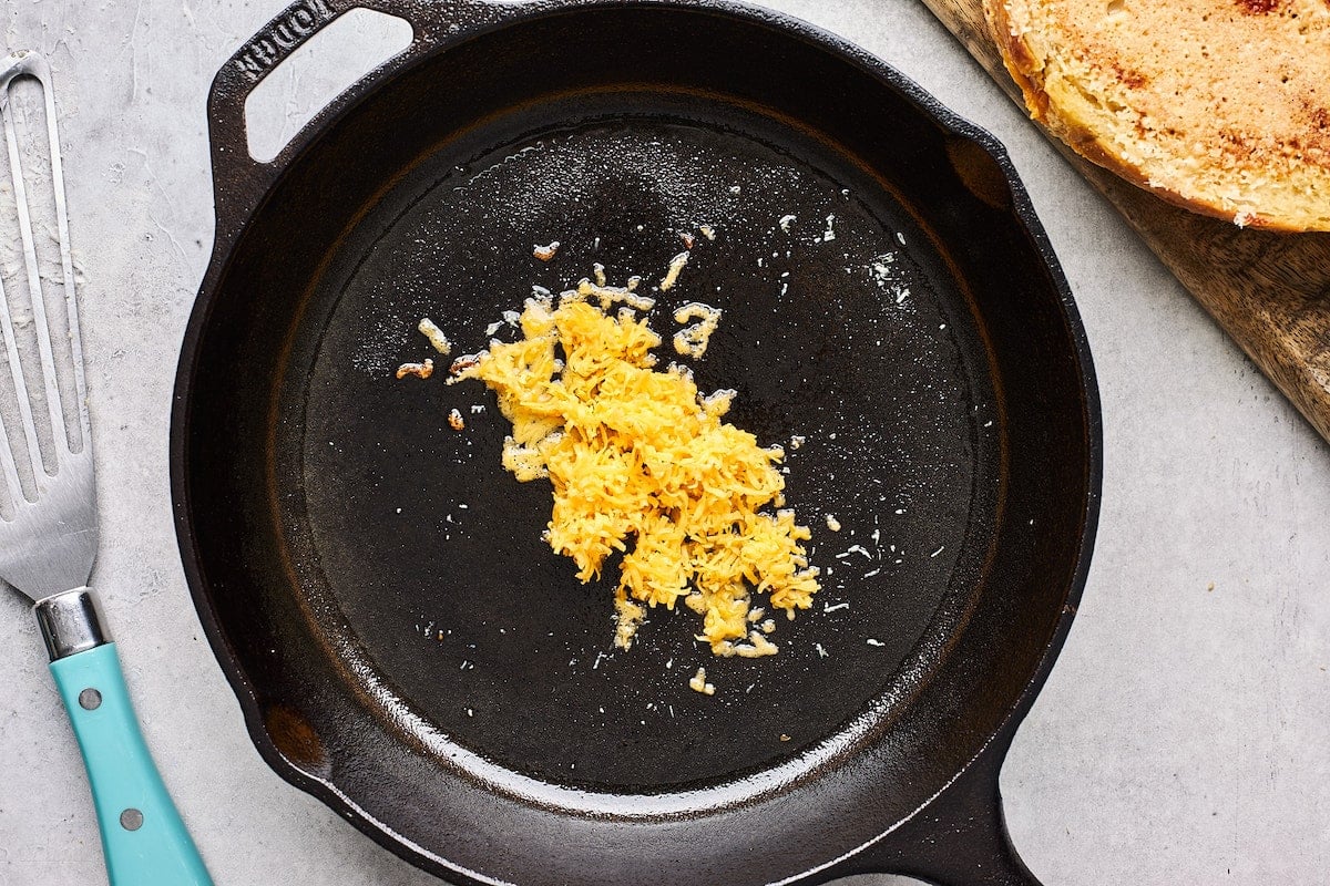 shredded cheddar cheese cooking in cast iron skillet to make cheese crust on grilled cheese.