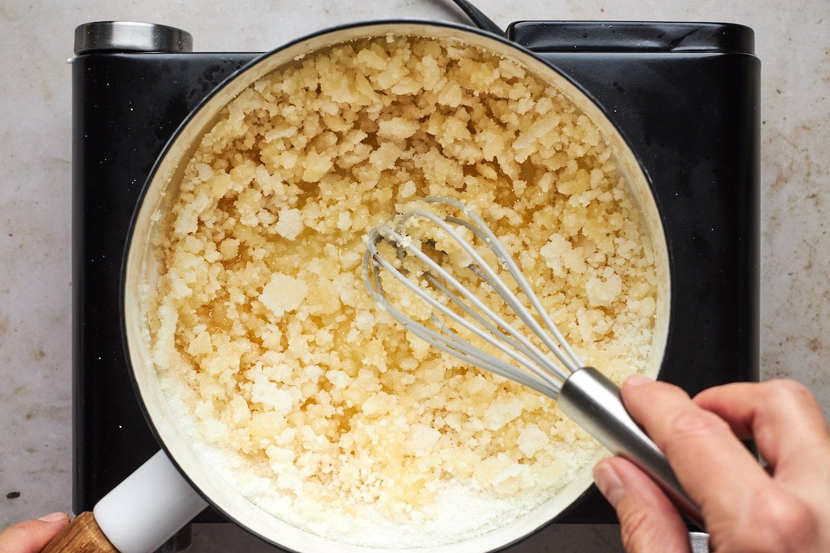 making salted caramel sauce with granulated sugar in pan on stovetop with whisk.
