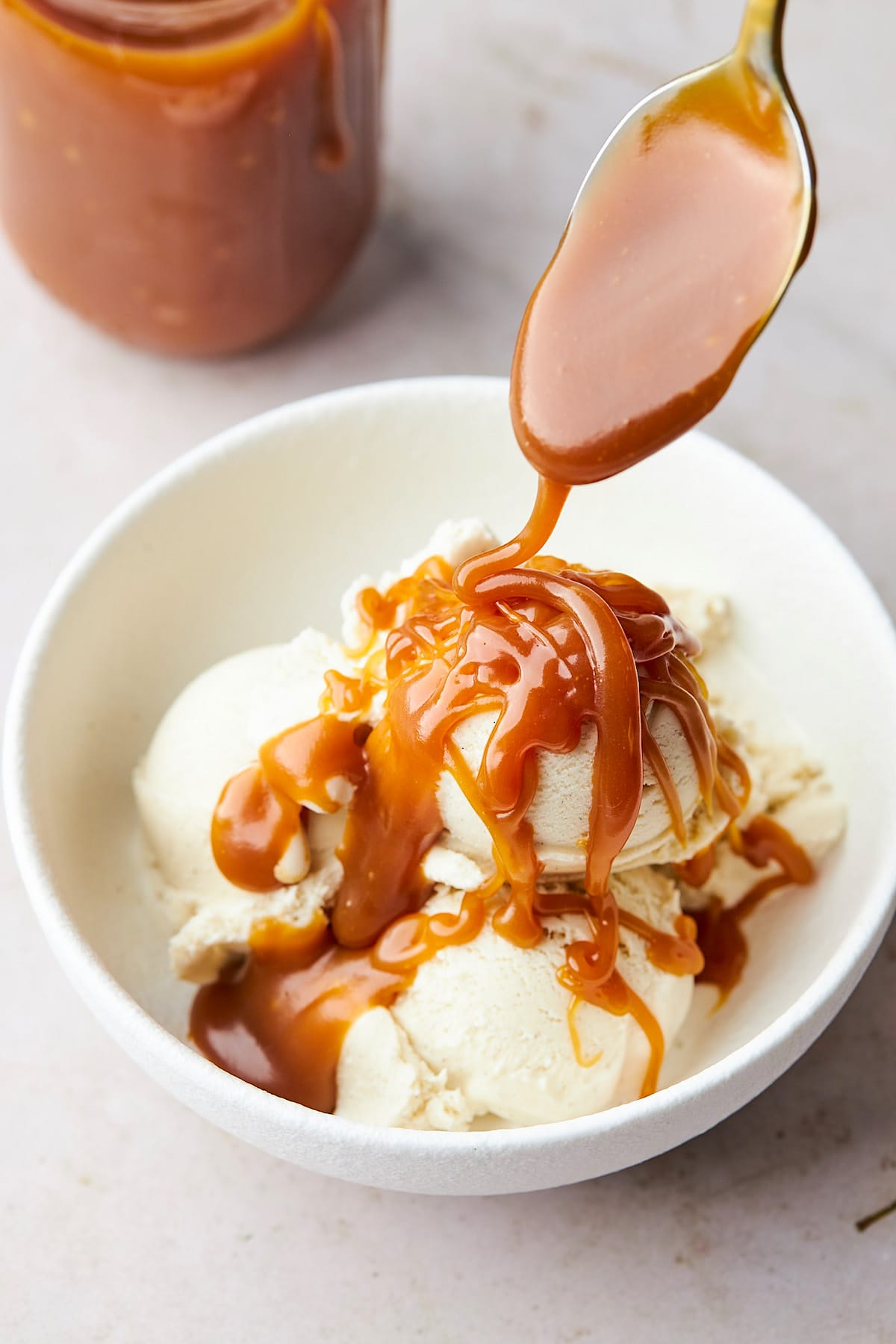caramel sauce being drizzled over vanilla ice cream with a spoon.