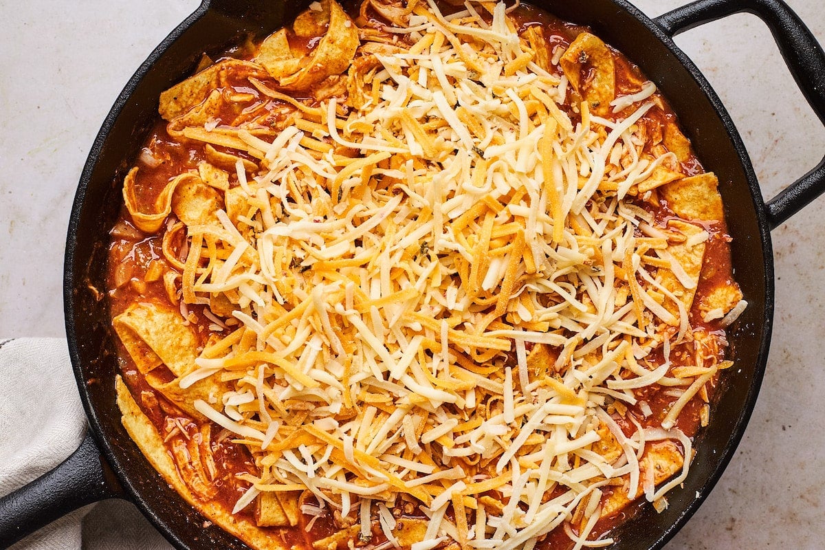 skillet chicken enchiladas topped with shredded cheese in cast iron skillet.