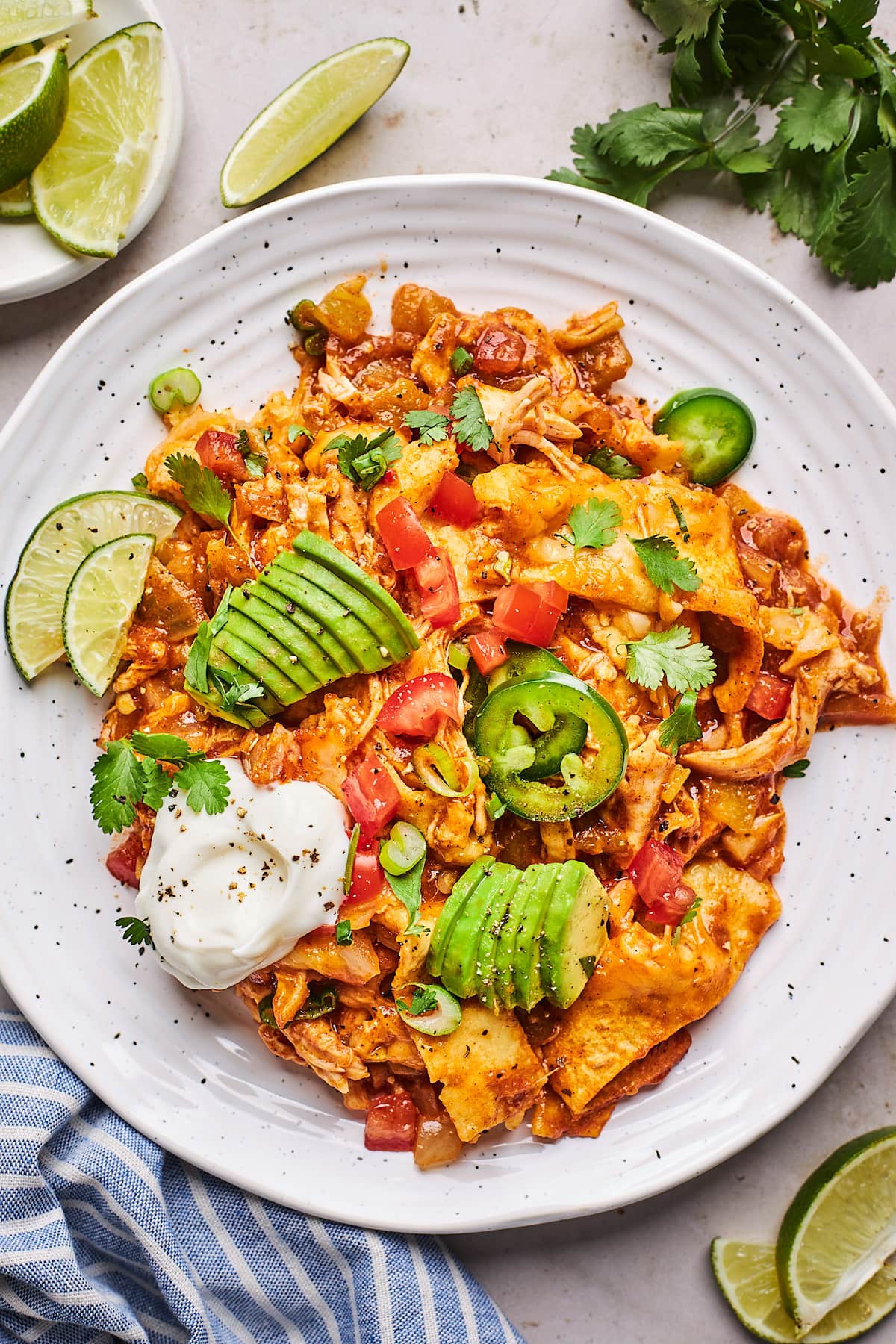 skillet chicken enchiladas on plate with sour cream, avocado, cilantro, tomatoes, and jalapeño slices.