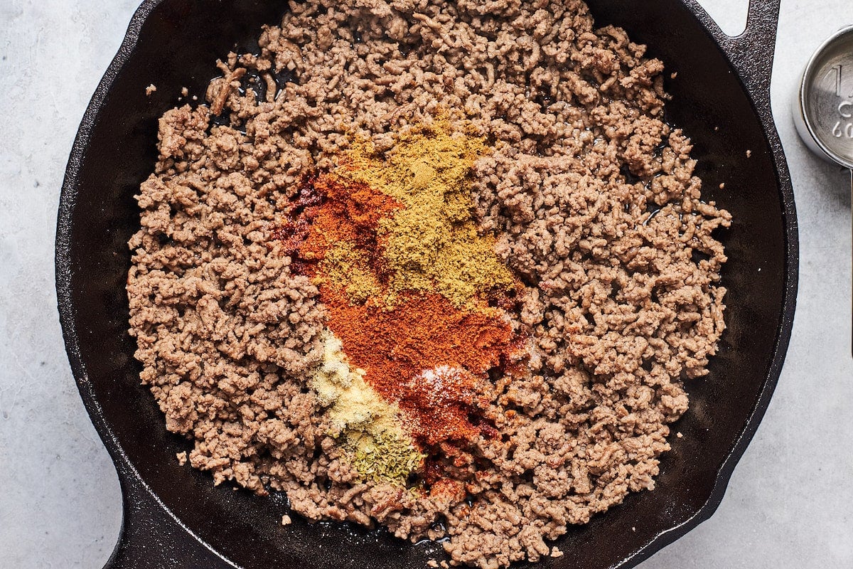 ground beef cooking in cast iron skillet with spices.