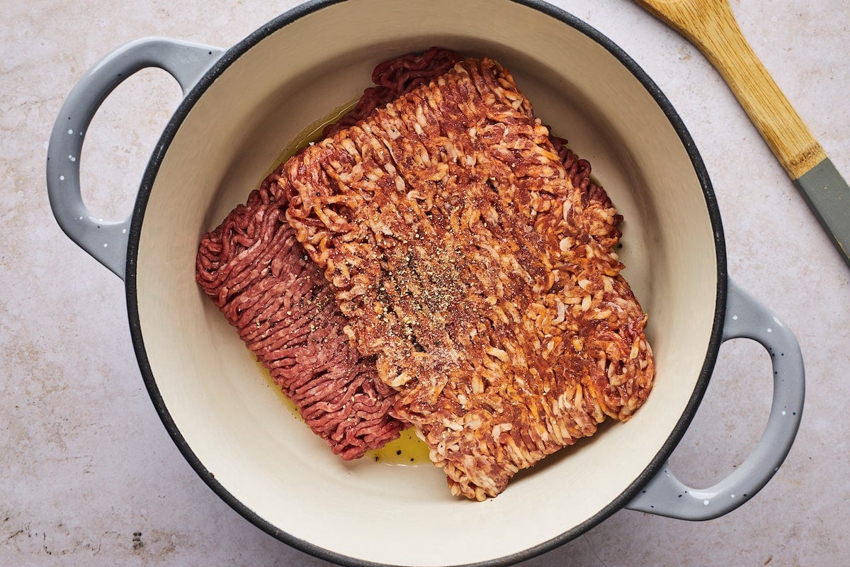 cooking ground beef and Italian sausage in large pot with wooden spoon.