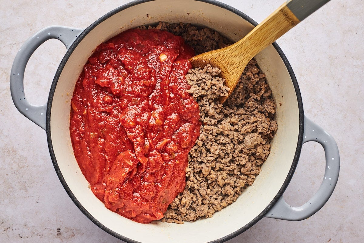 cooking ground beef and Italian sausage with marinara sauce in large pot with wooden spoon to make lasagna.