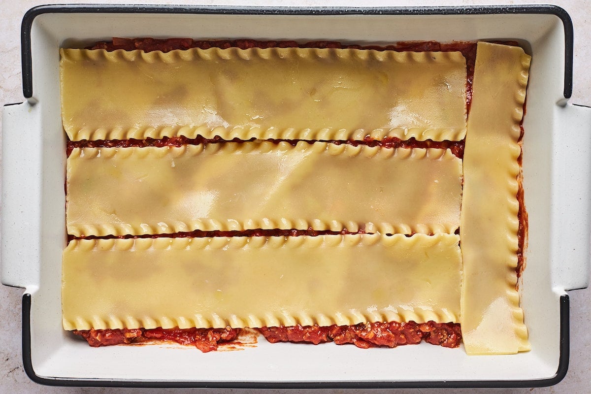 layering meat sauce and cooked lasagna noodles in baking pan.