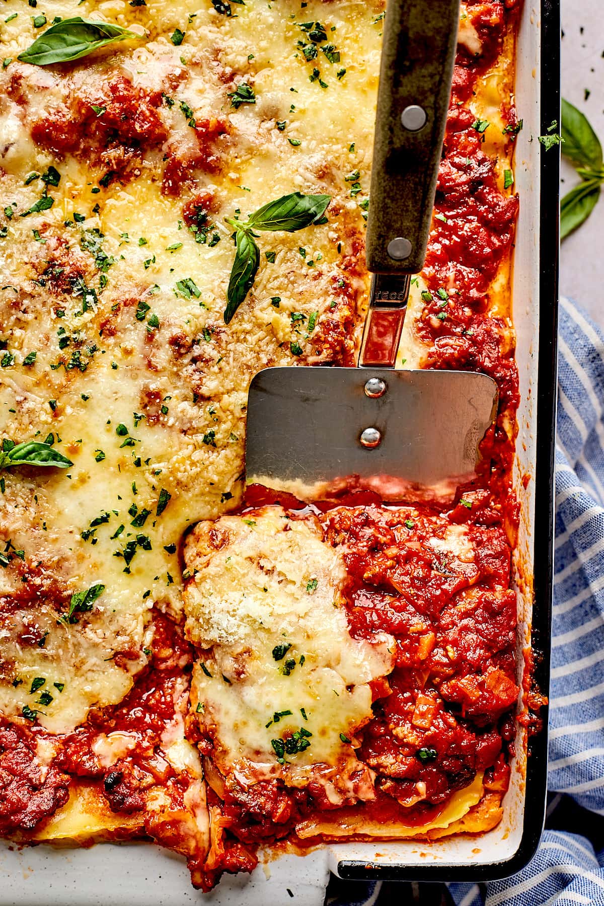 a cut piece of lasagna in baking pan with a metal spatula.