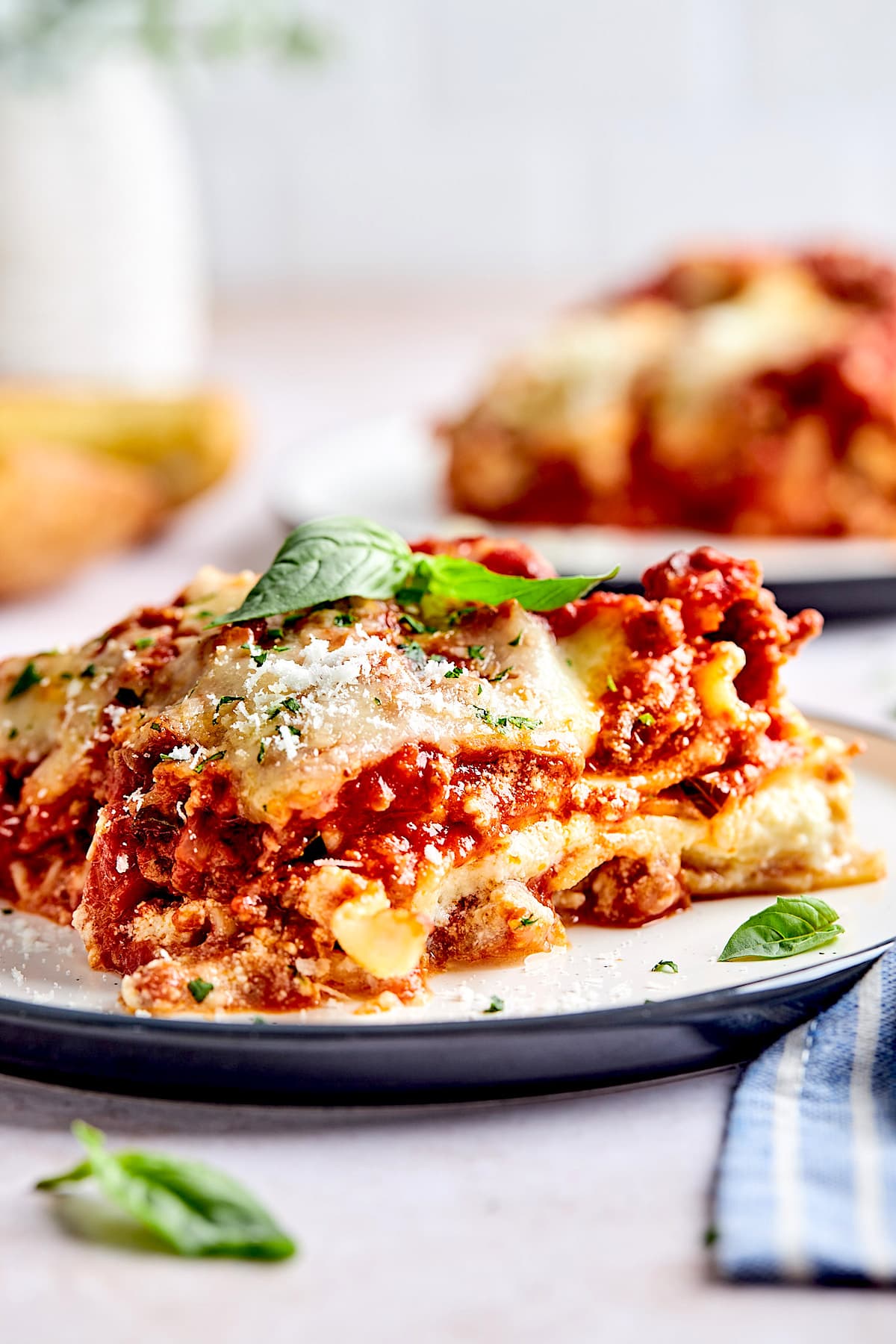 piece of homemade lasagna on plate garnished with fresh basil and Parmesan cheese.