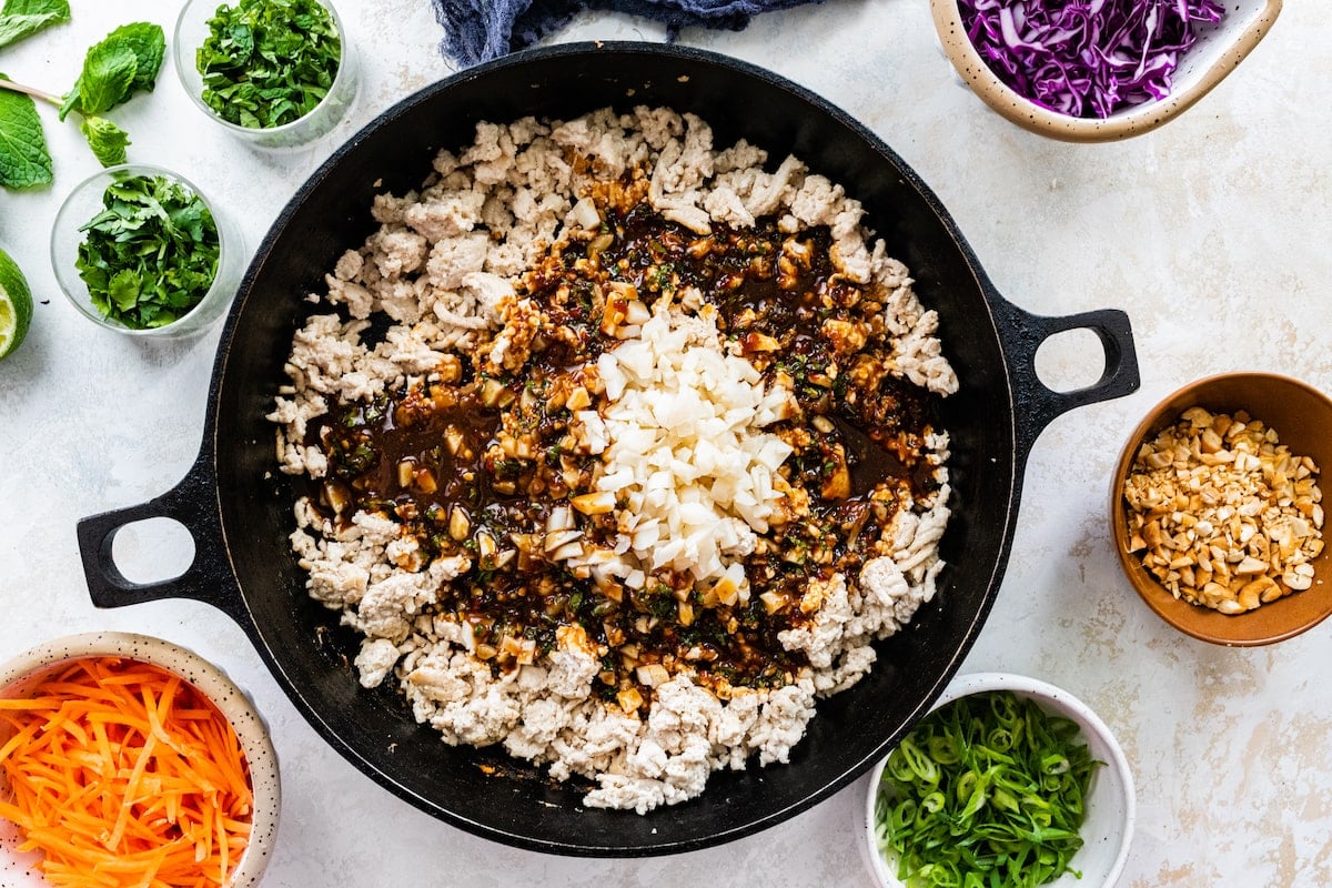 ground chicken with sauce and chopped water chestnuts being cooked in cast iron skillet.