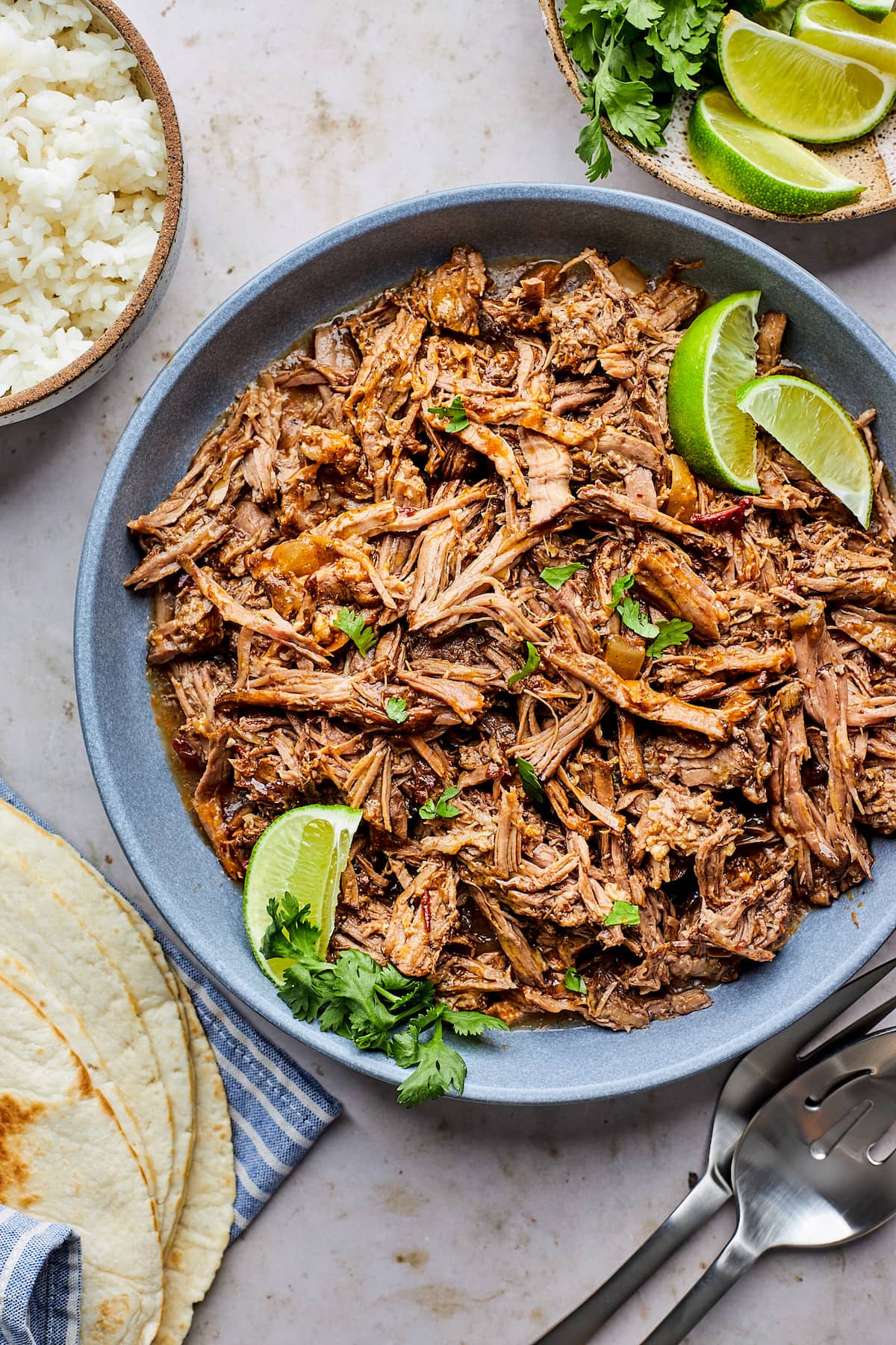 shredded Barbacoa in blue bowl with lime wedges and cilantro.